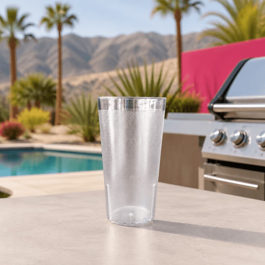 Pebbled tumbler staged beside an outdoor grill with pool backdrop